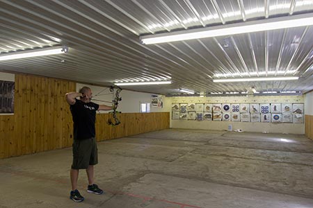 An archer at full draw on the indoor range at Straight Arrow Archery